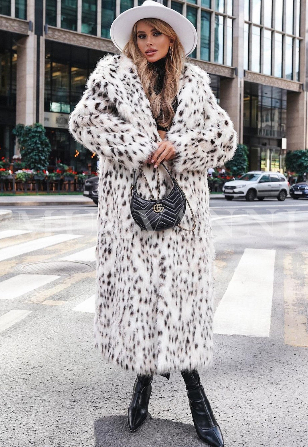 Woman wearing JOVANNA long premium white leopard print faux fur coat, styled with black boots and a chic hat in a city setting.