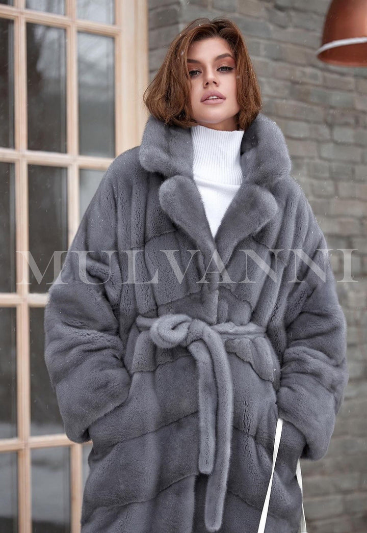 A woman in a sleek long grey mink fur coat, highlighting its luxurious softness and graceful silhouette. The coat's timeless style adds a touch of sophistication to her winter wardrobe.